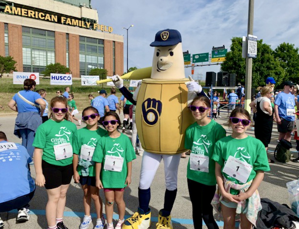 Some College Park Girls on the Run team members pose with a Brewers mascot at AmFam Field..
