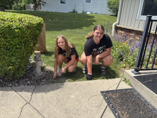Two students crouched along a walkway pulling weeds.