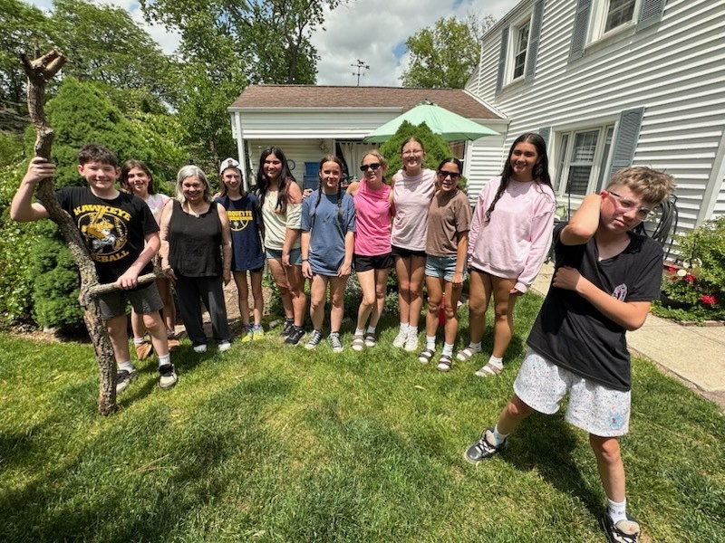 A group of students smiling and posing in a yard after helping the owner with spring chores.