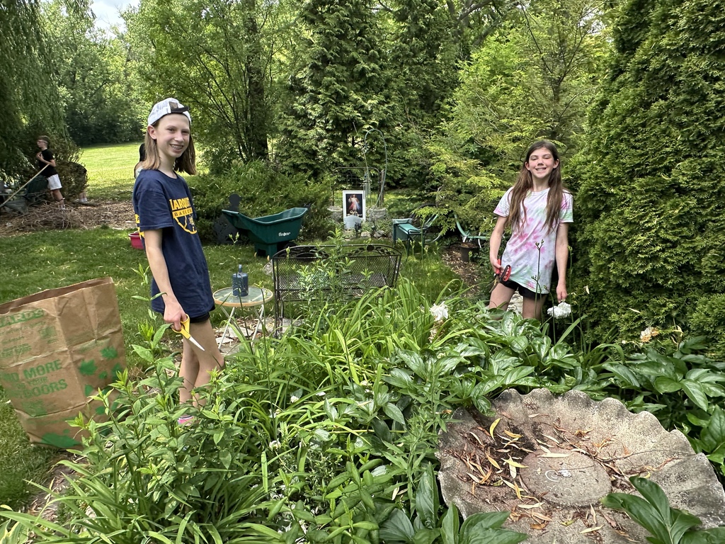Two students smiling and standing in a garden trimming plants.