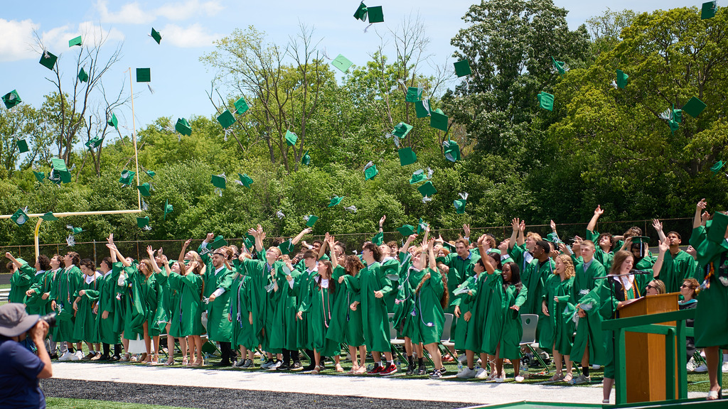 Students wearing green gowns tossing up their graduation caps.