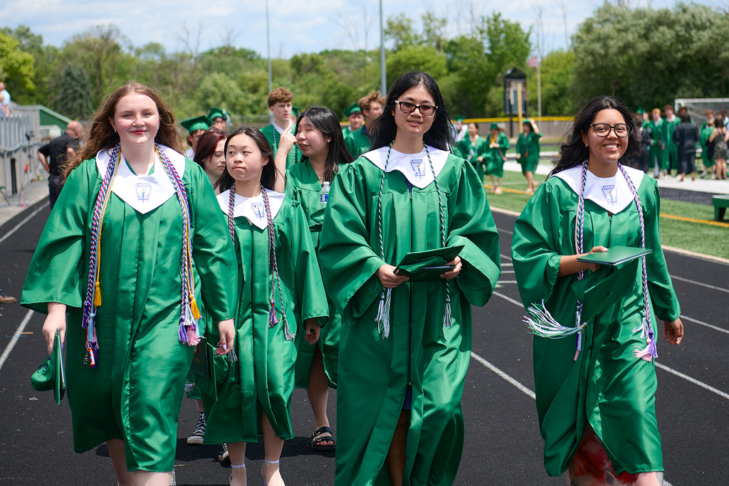 Students wearing green caps and gowns walking out of a stadium.
