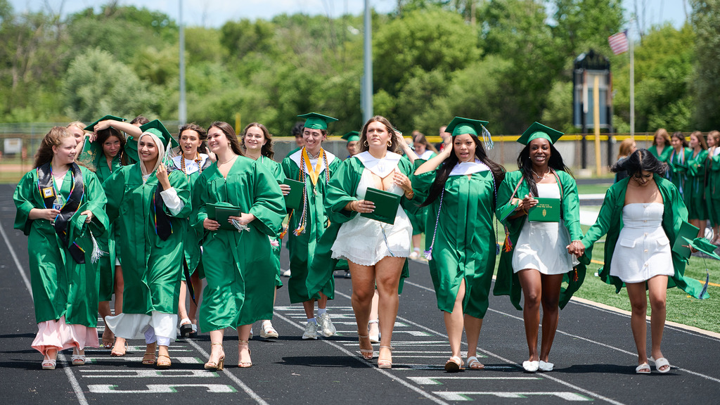 Students wearing green caps and gowns walking out of a stadium.