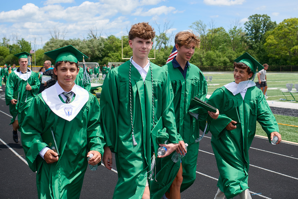 Students wearing green caps and gowns walking out of a stadium.