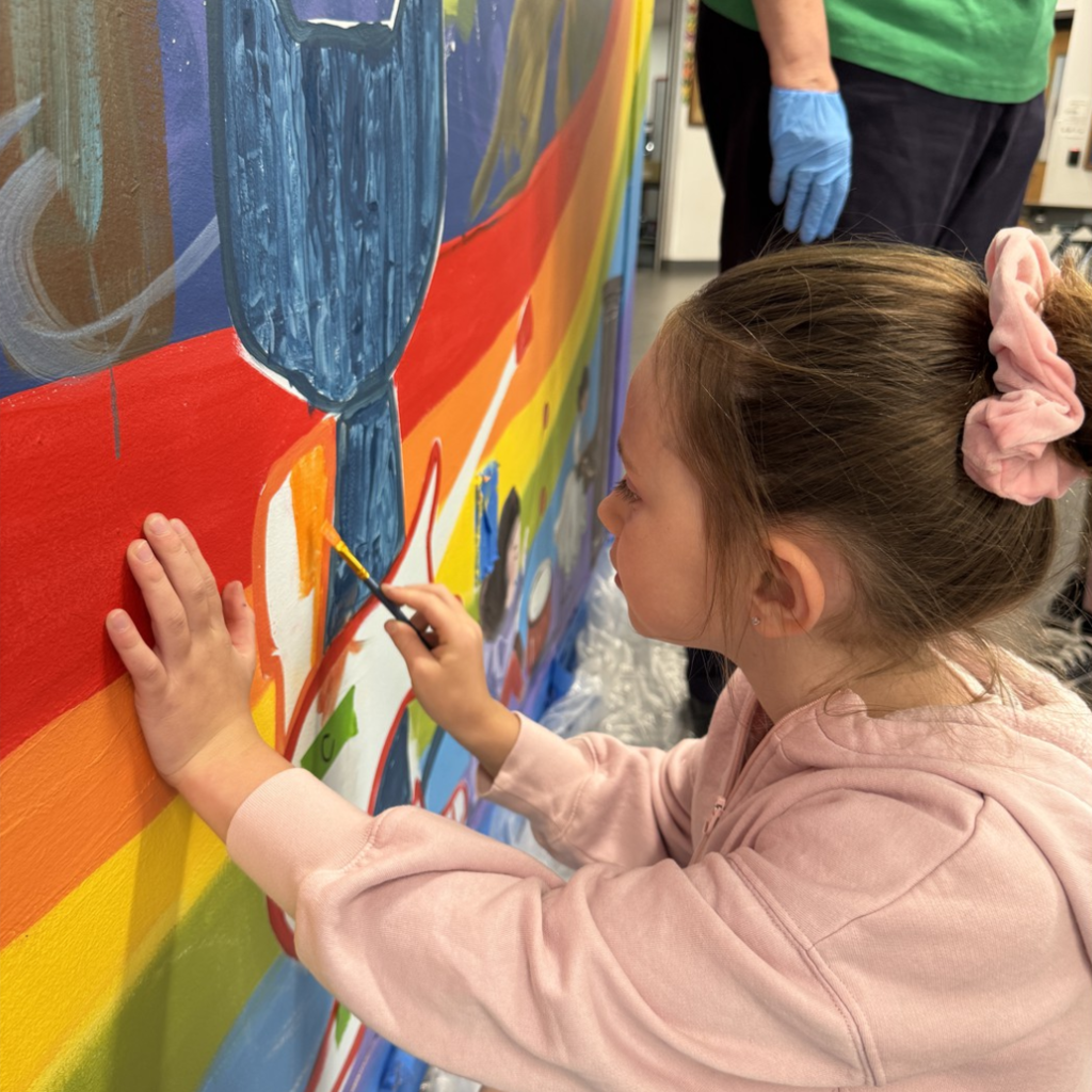 Close up image of a student with a paint brush in hand painting on the school mural.