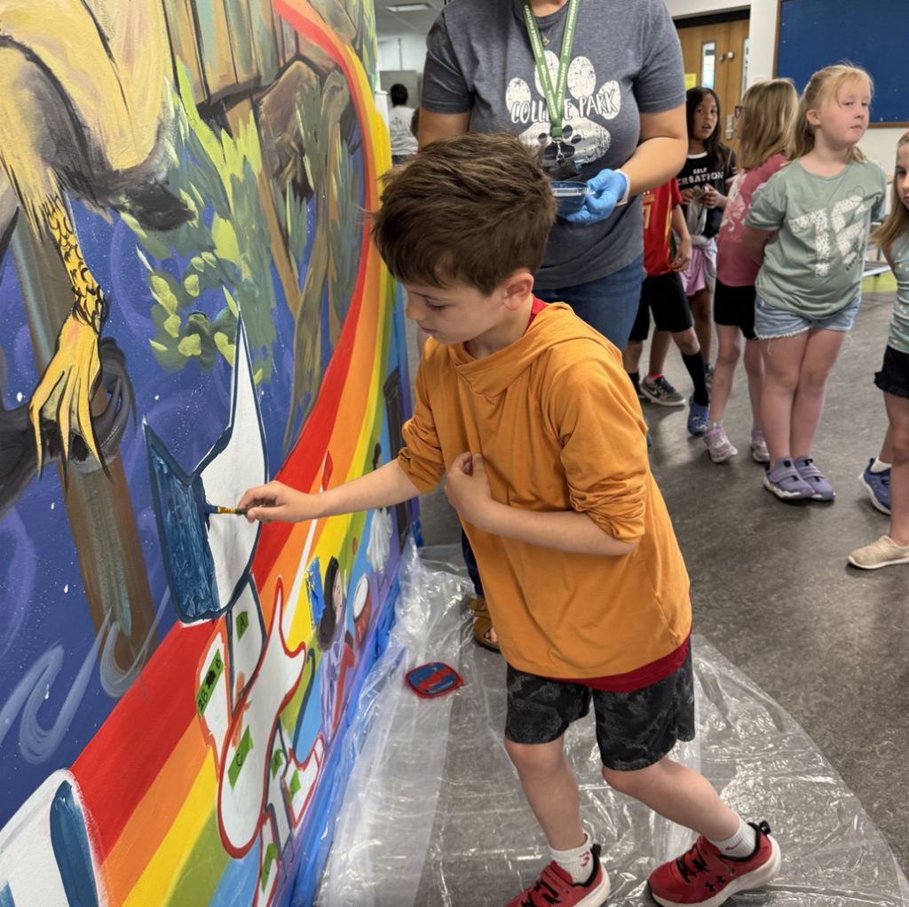 A student with a paint brush in hand painting on the school mural.