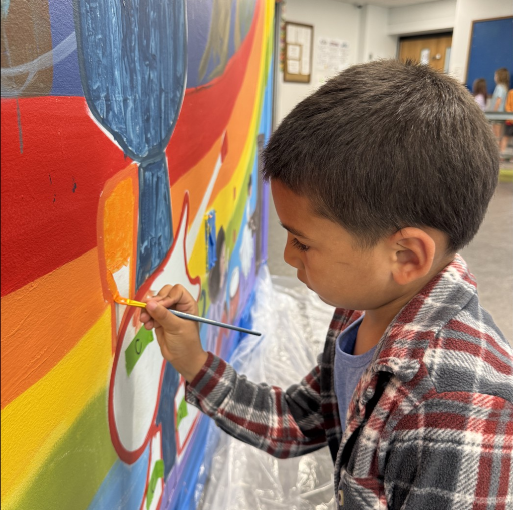 Close up image of a student with a paint brush in hand painting on the school mural.