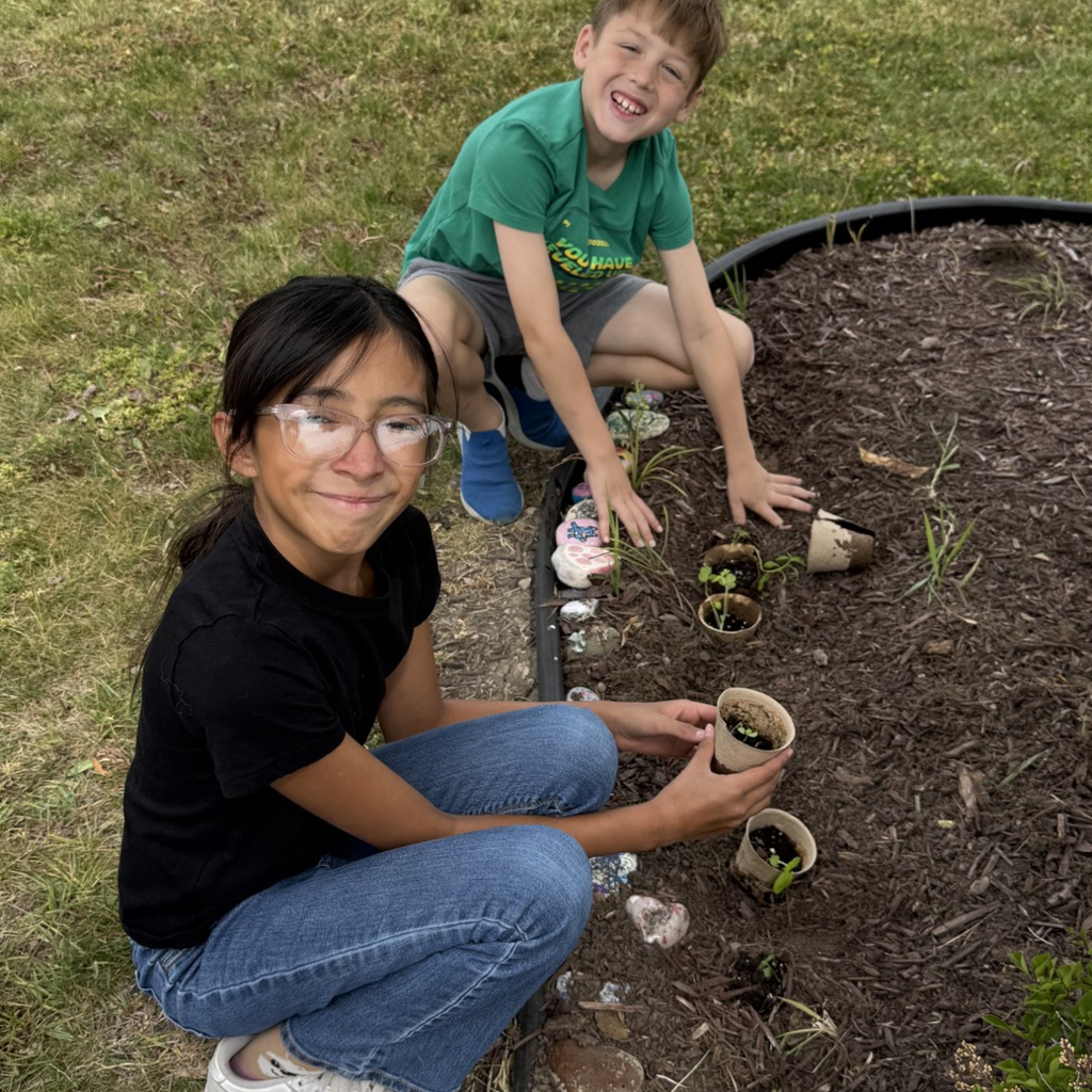 Two students smiling and working in the school gardens with little plants.