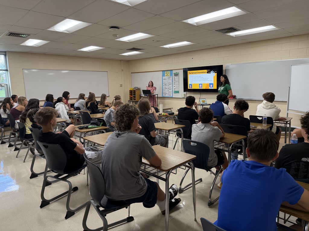 Two people standing in front of a group in a classroom introducing the students two the school guidance team.