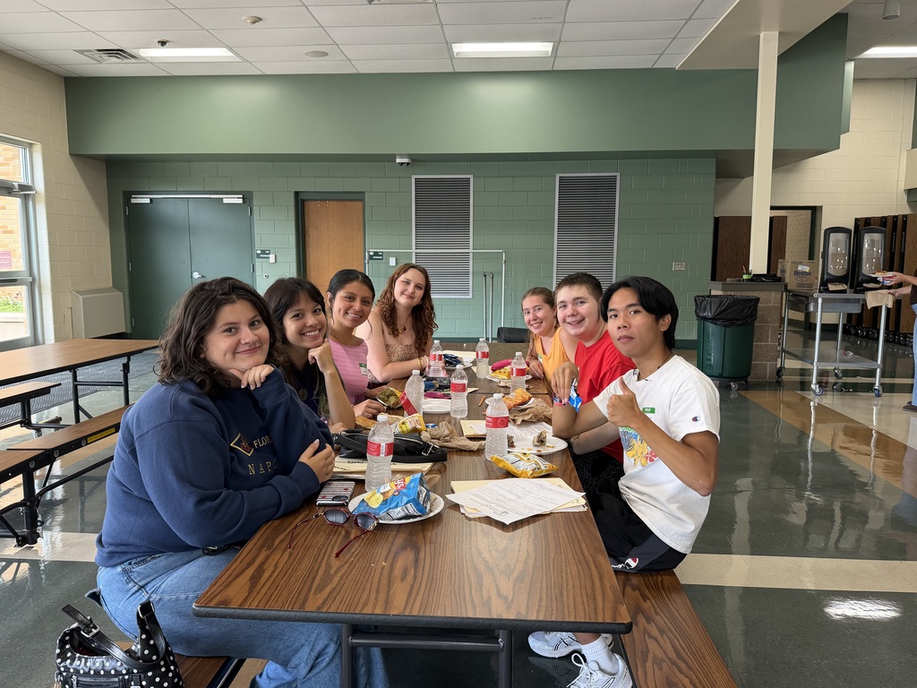 Students sitting at a lunch table smiling at the camera