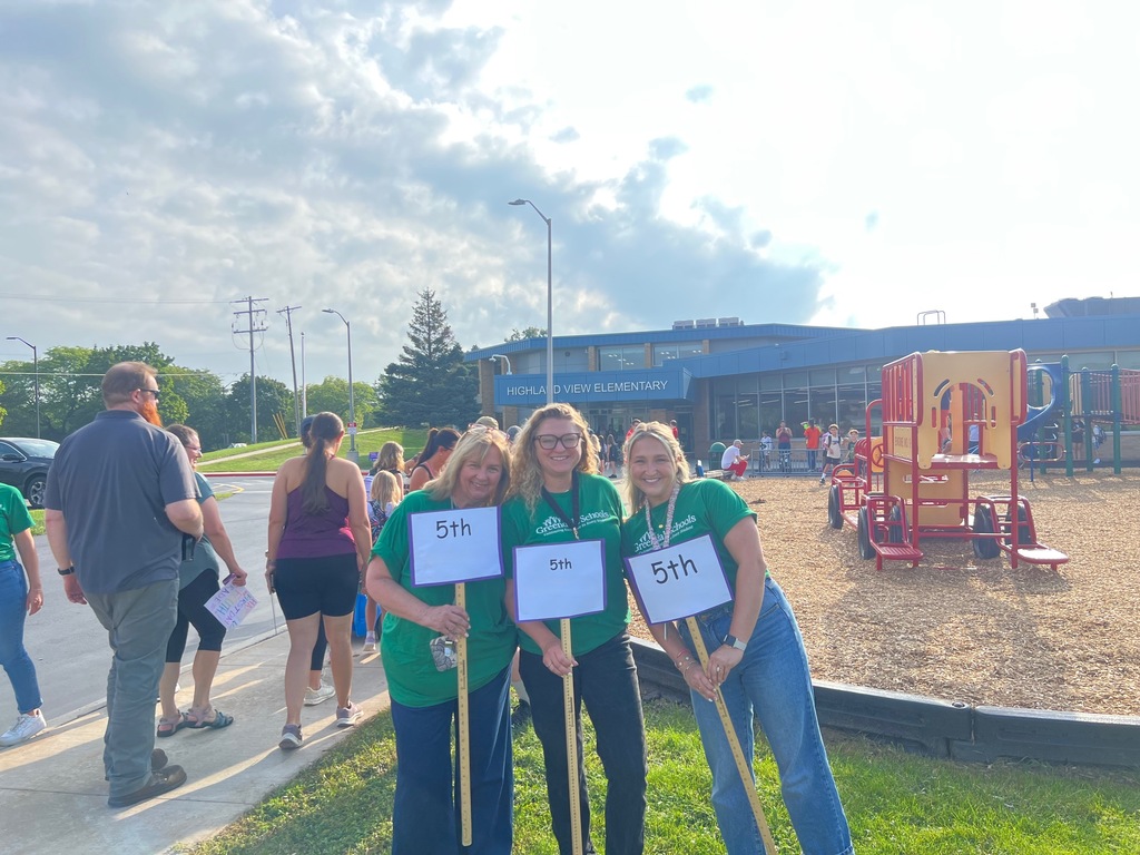 Three teachers wearing matching green shirts standing in front of a playground a a school named Highland View.