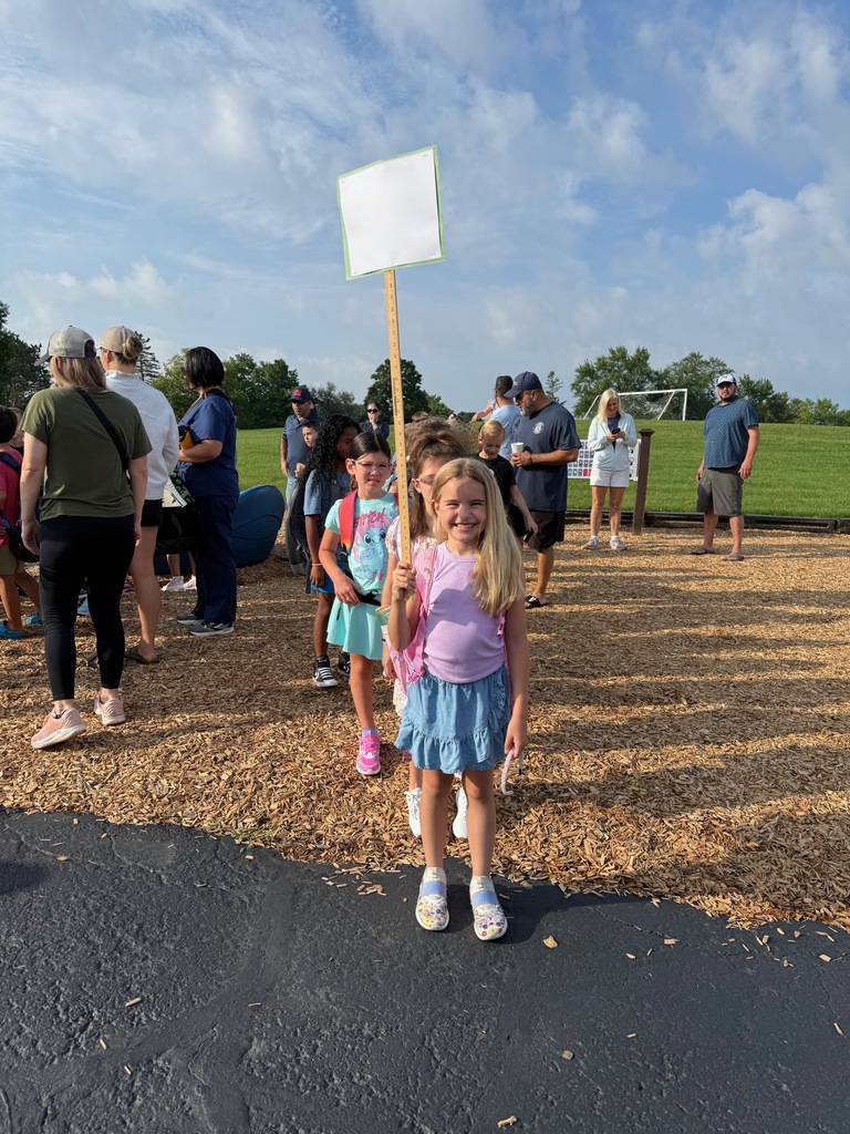 Students smiling and looking toward the camera on the playground with parents in the background