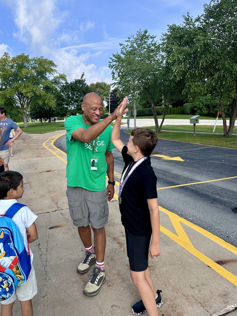Principal Brock giving a student a high five on the sidewalk in front of the school on the first day.