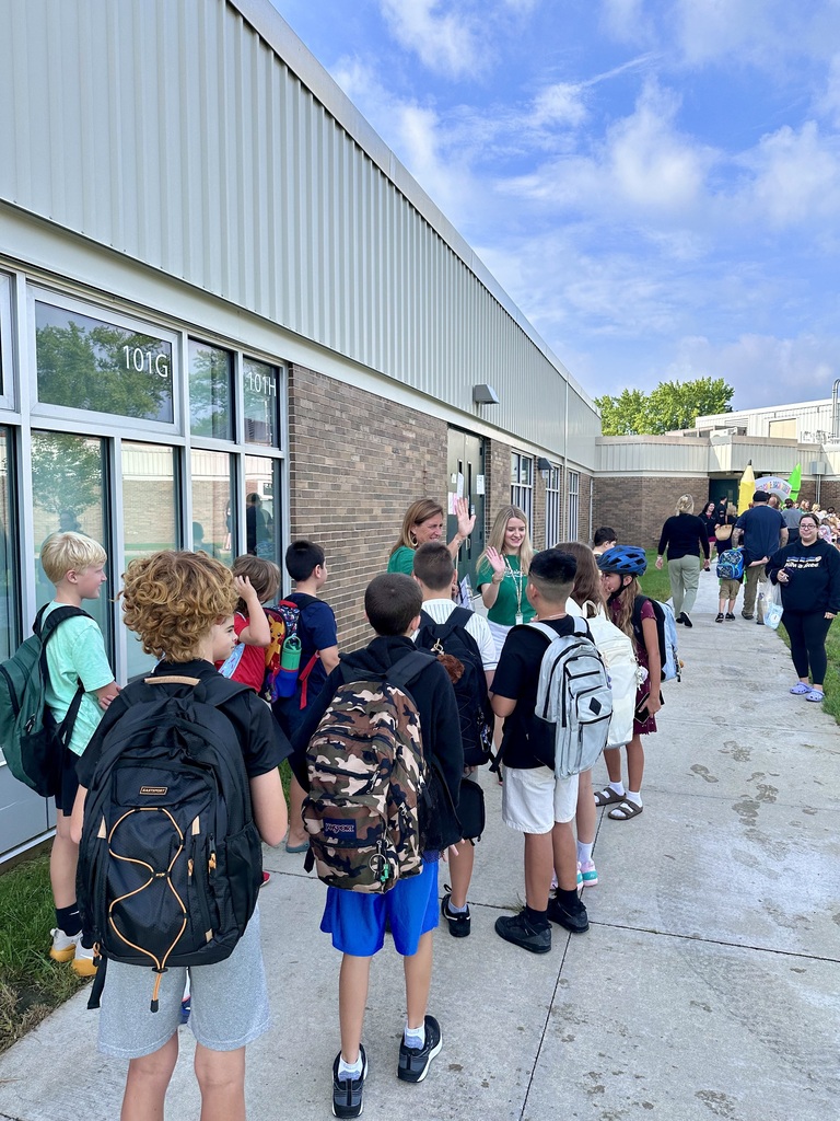 Two teachers out in front of school greeting students with waves and high-fives.