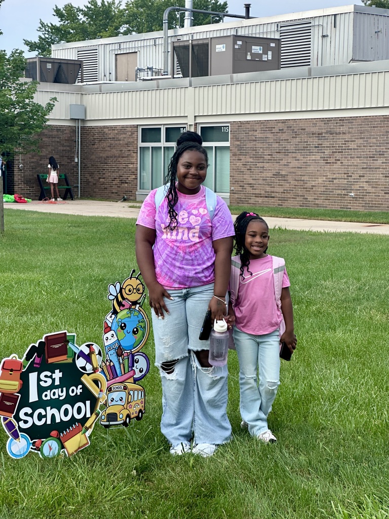 Two smiling sisters posing in front of the school.