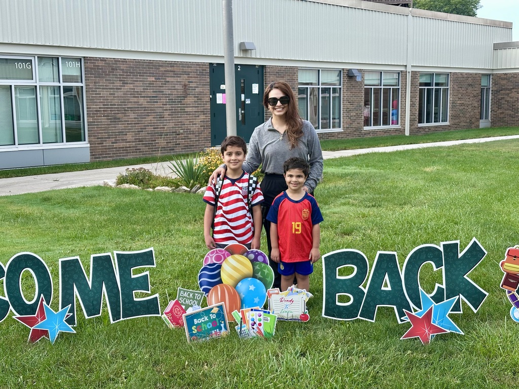 A mom and her two boys smiling and posing in front of the school on the first day.