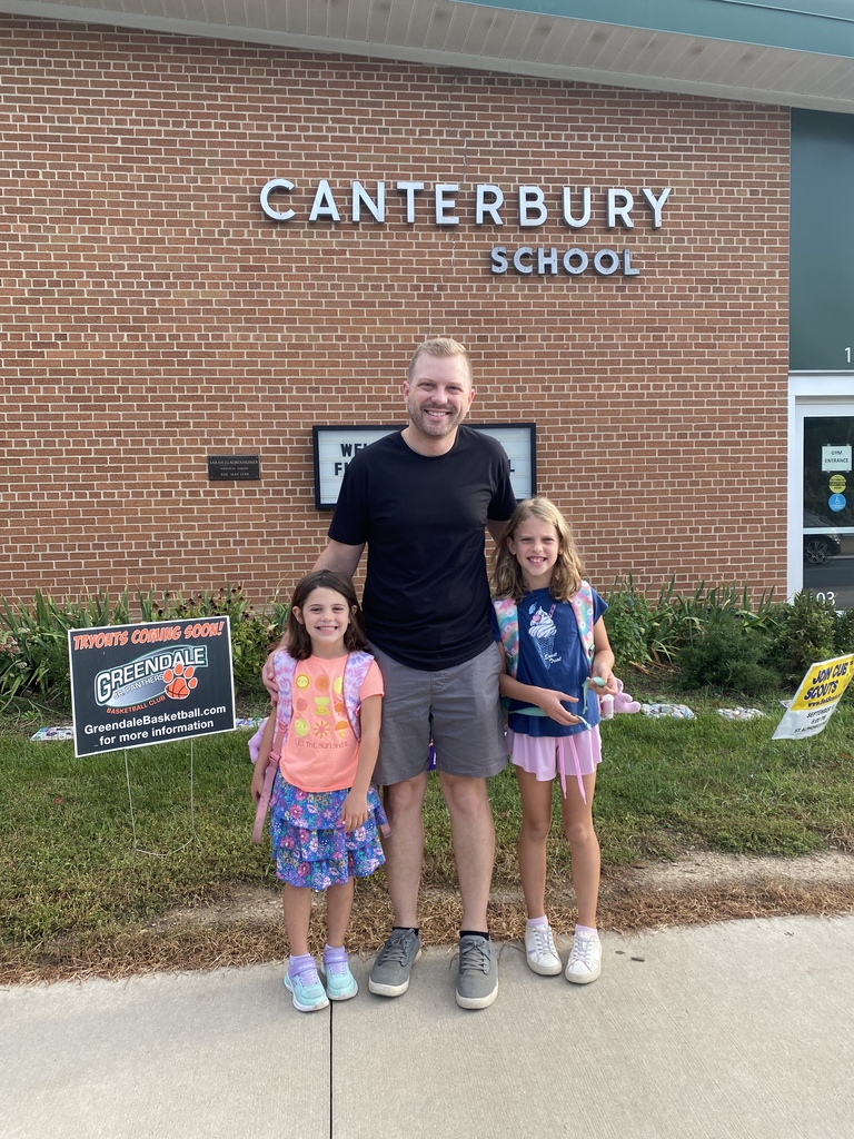 Man and two students posing in front of the school sign.