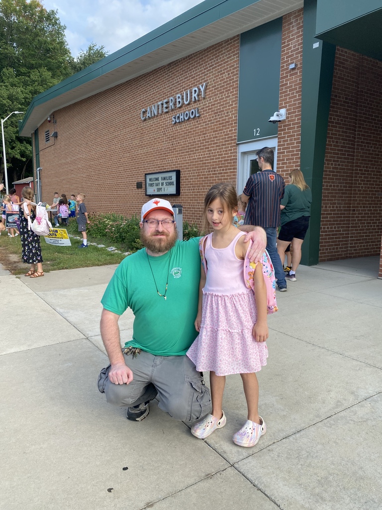 Man and child posing for a photo in front of the school sign.