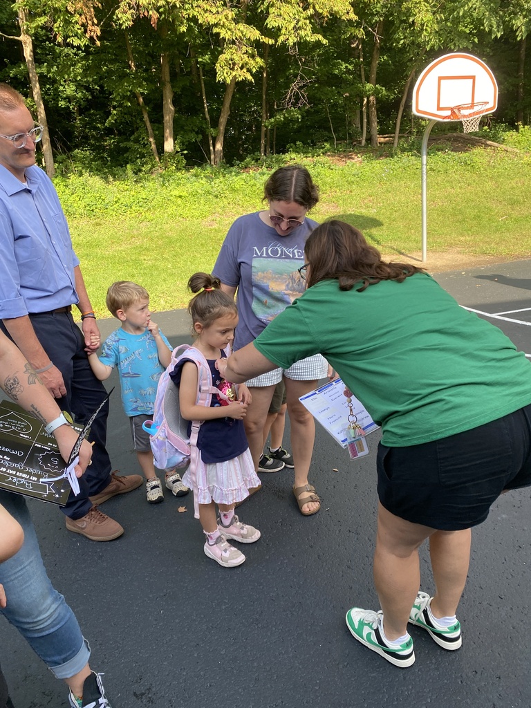 Teacher putting a name tag on a student as parents, sibling look on. 