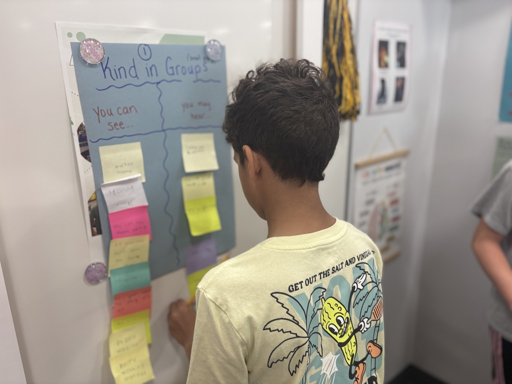 Student looking at a bulletin board and posting a note about kindness