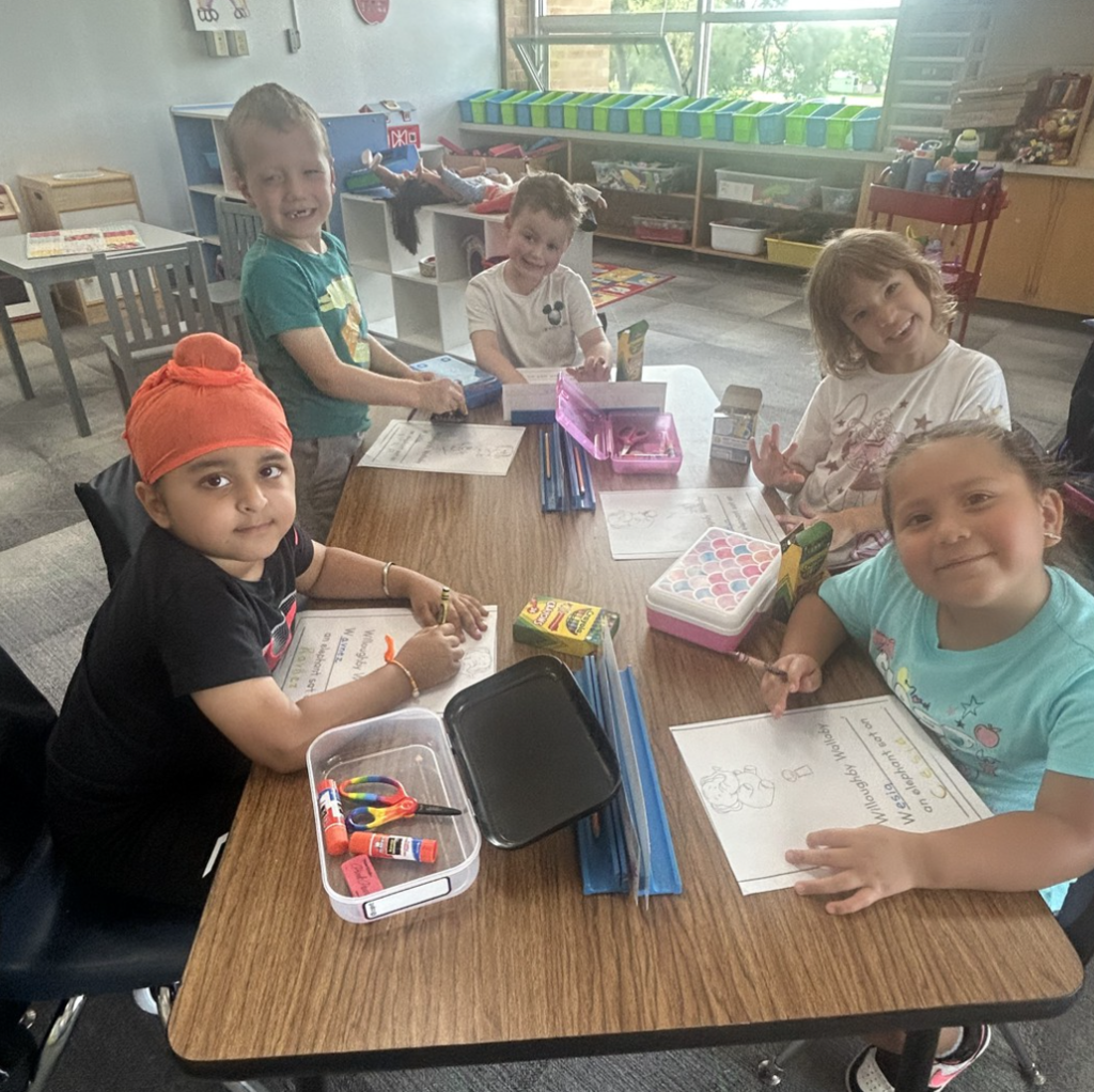 Five 5K students sitting at a table with papers in front of them smiling and working on a project.