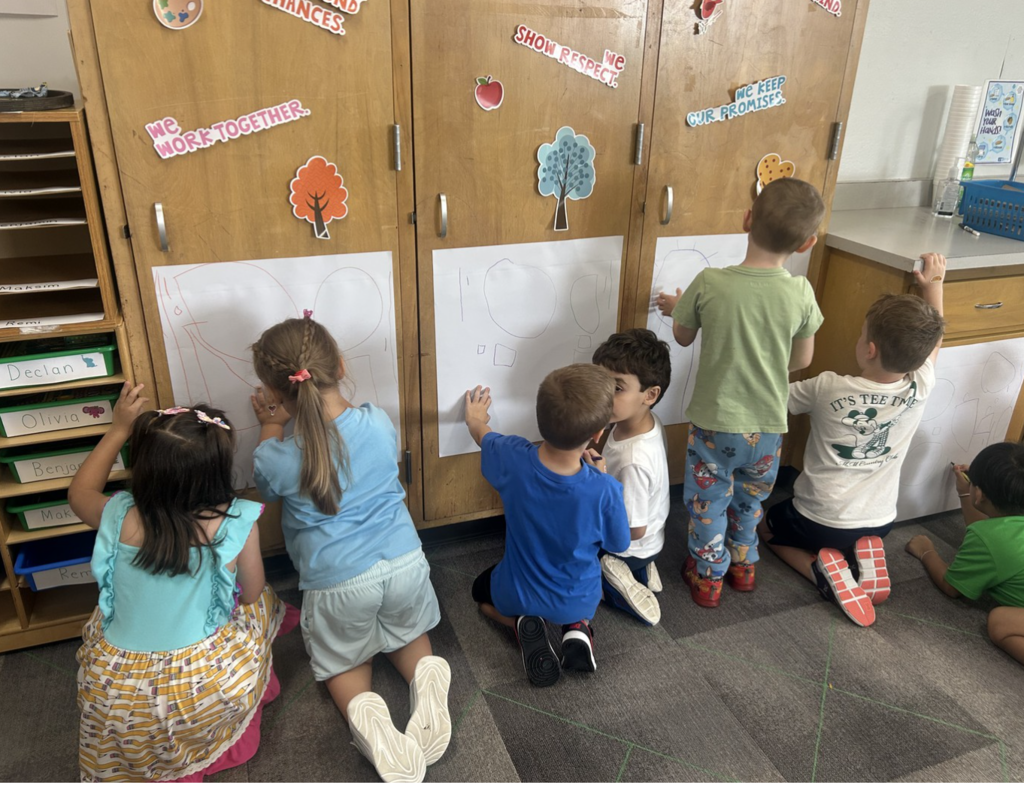 5K students working in pairs writing on large paper taped on cabinets.