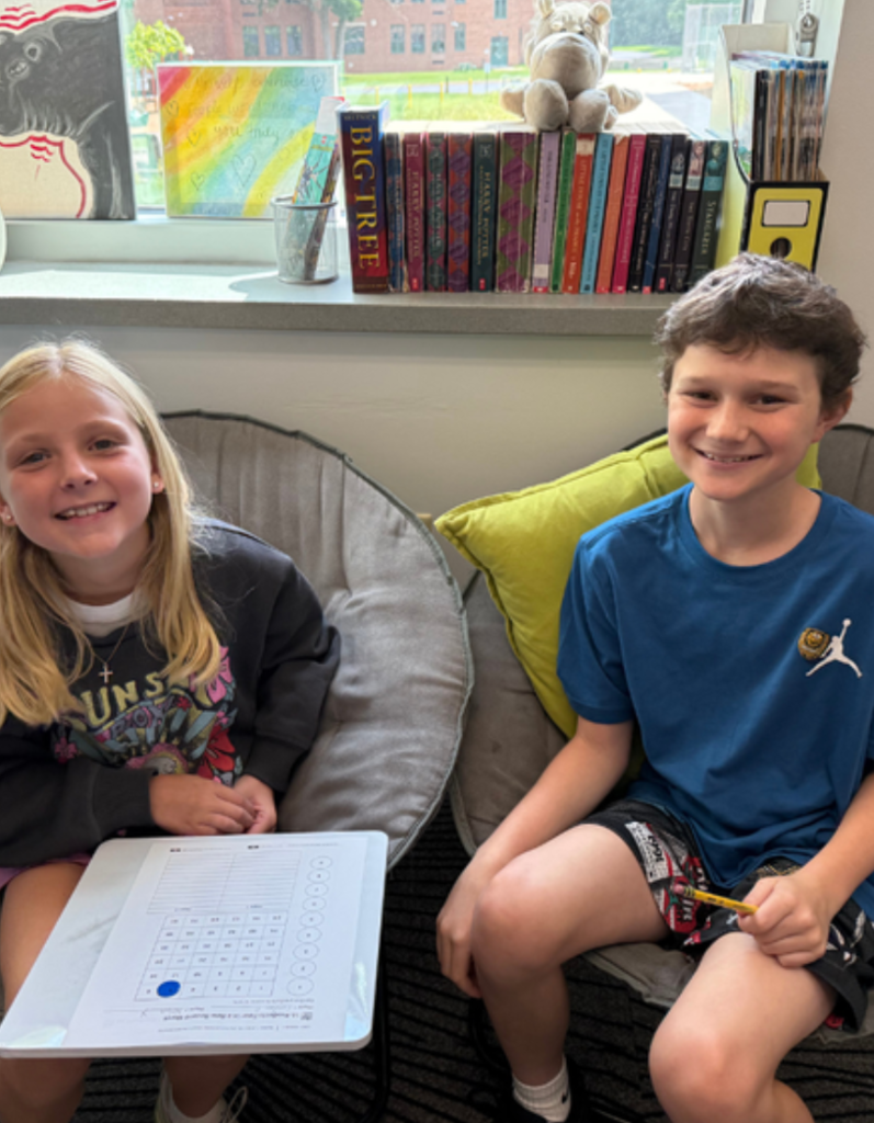 Two fifth grade classmates smile while working on a classroom scavenger hunt.