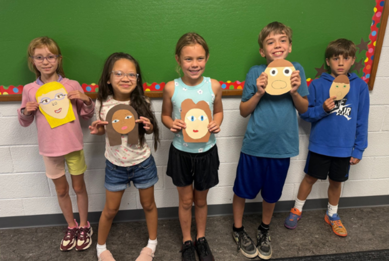 Five students posing and holding their self-portraits.