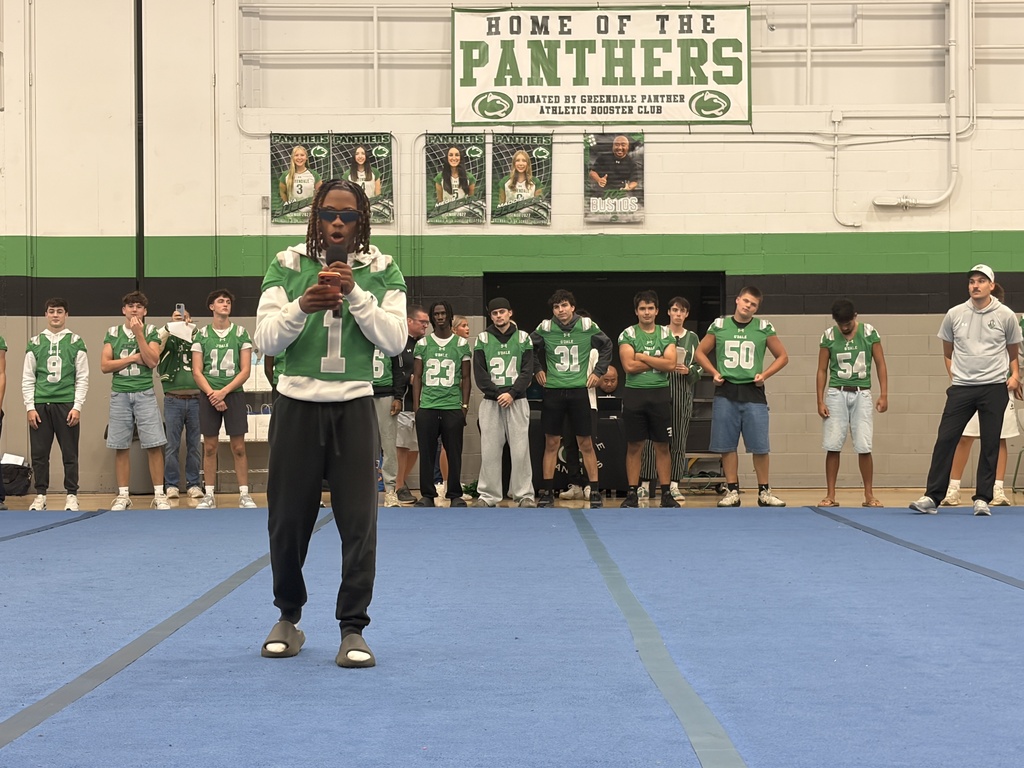 A football player reading a welcome message the the crowd off of his phone with other players standing behind him
