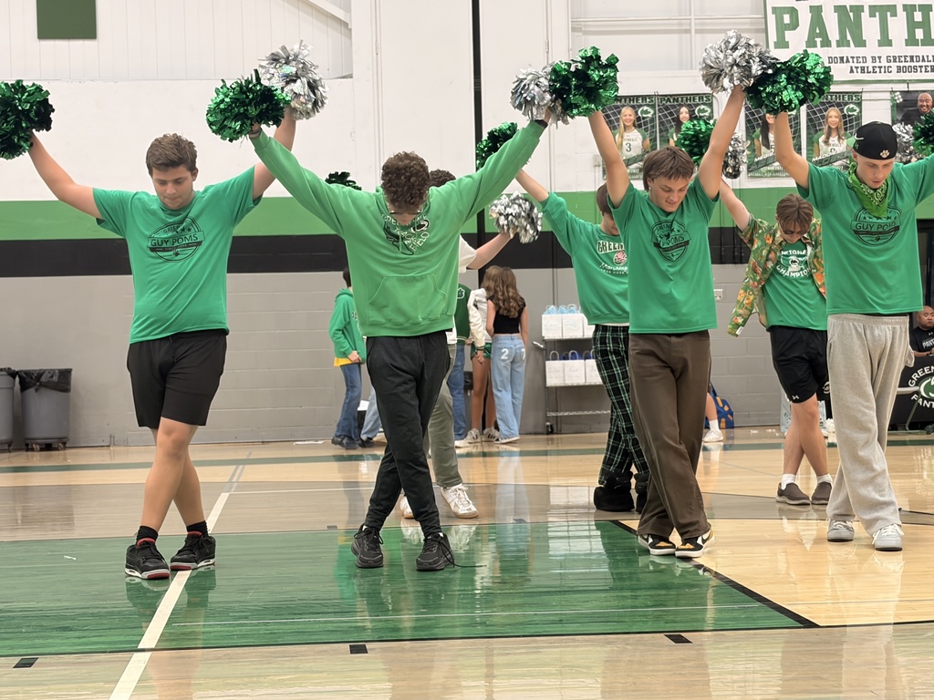 Boys standing with legs crossed and holding pom pons during a dance