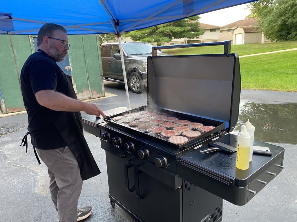 A person grilling burgers outdoors under a canopy