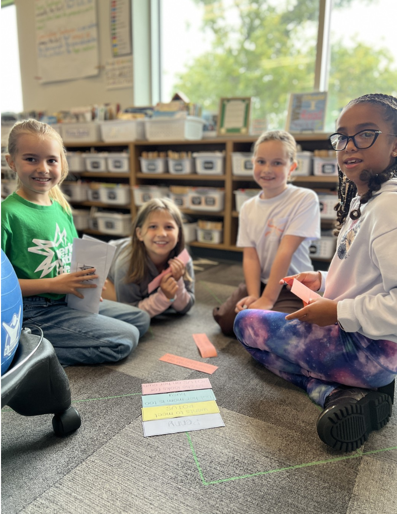 Four third graders smile and pose as they work on story summaries.