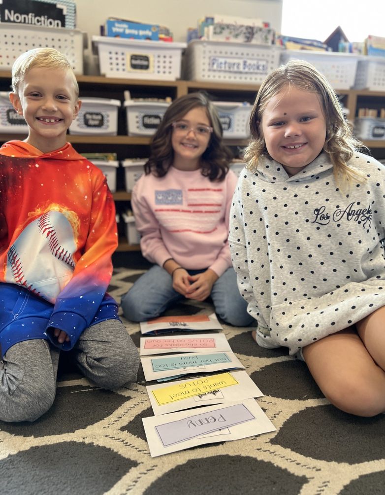 Three smiling third graders pose as they work on story summaries.