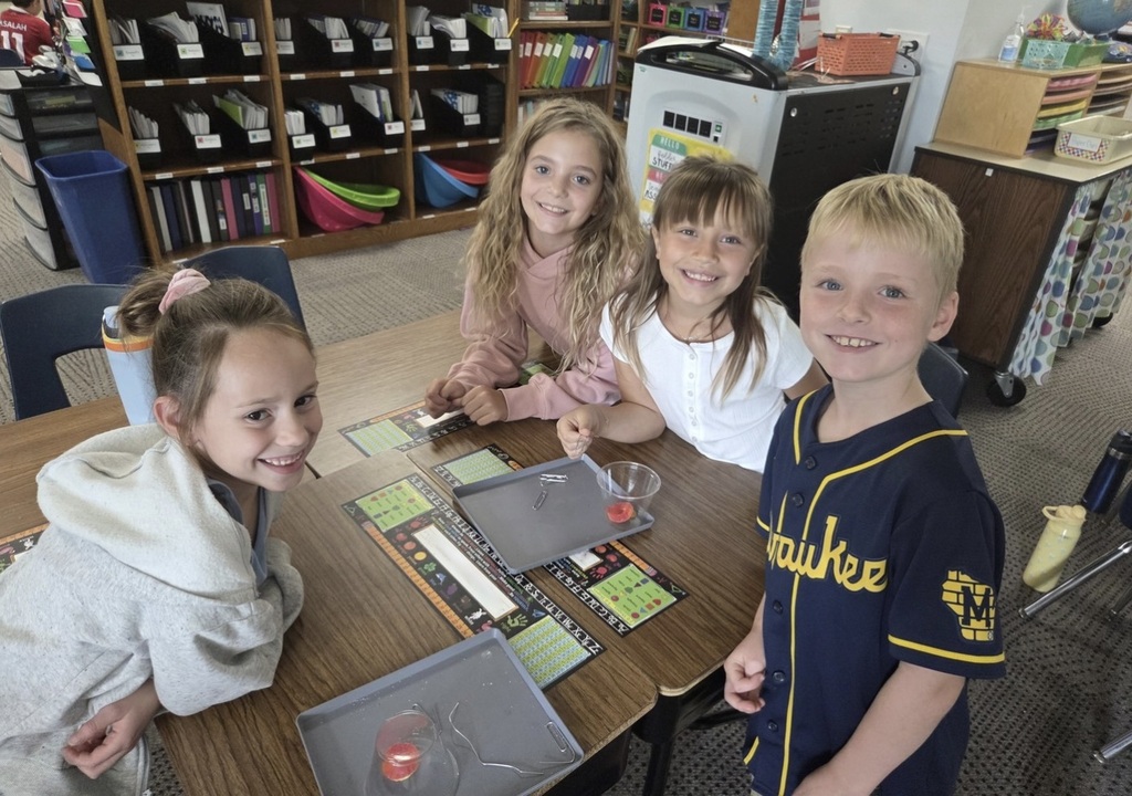Four second graders smiling while working closely together around a desk.