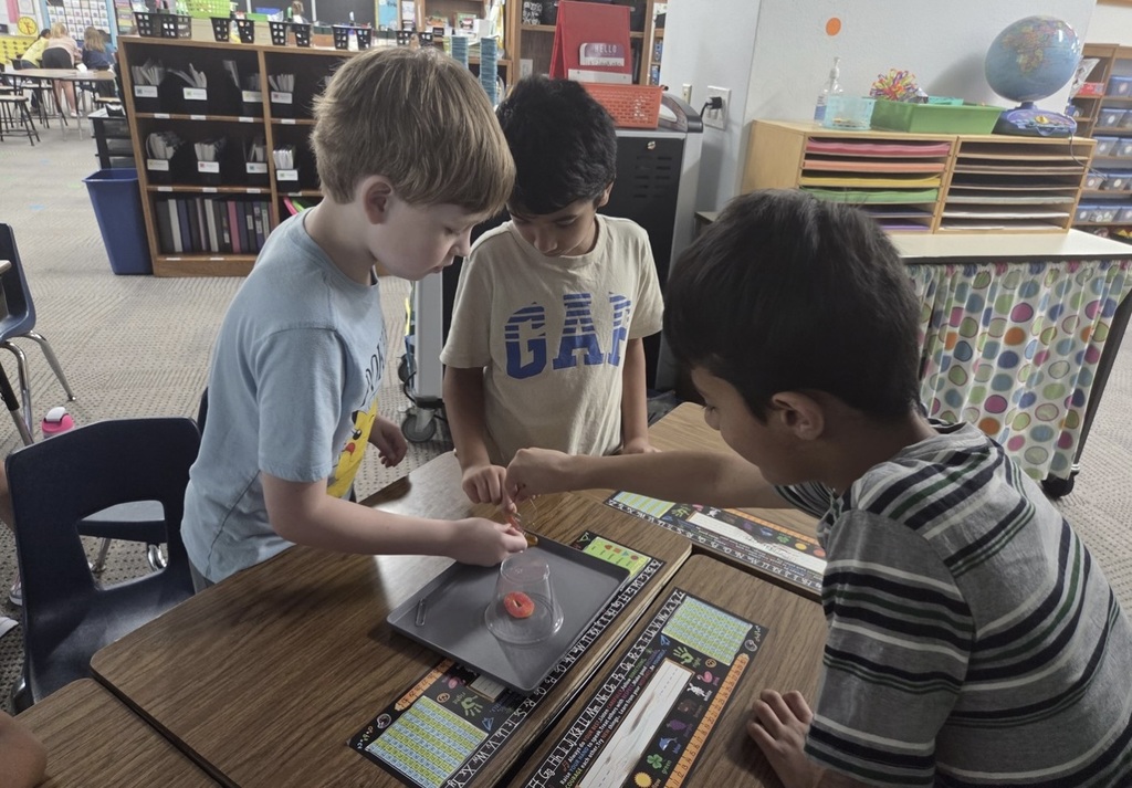 Three second graders working closely together around a desk.