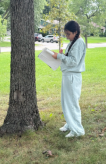 A fifth graders outside by a tree with a notebook in a sensory walk to expand descriptive writing skills.