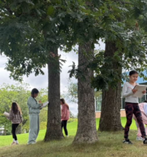 Fifth graders outside with notebooks doing a sensory walk to expand their descriptive writing skills.
