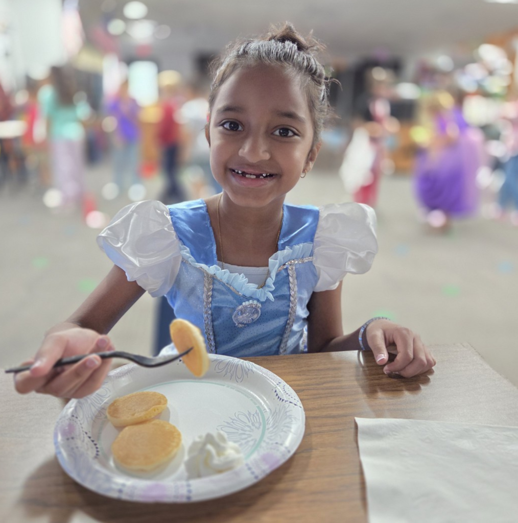  Student dressed as a princess smiles with a plate of mini pancakes.