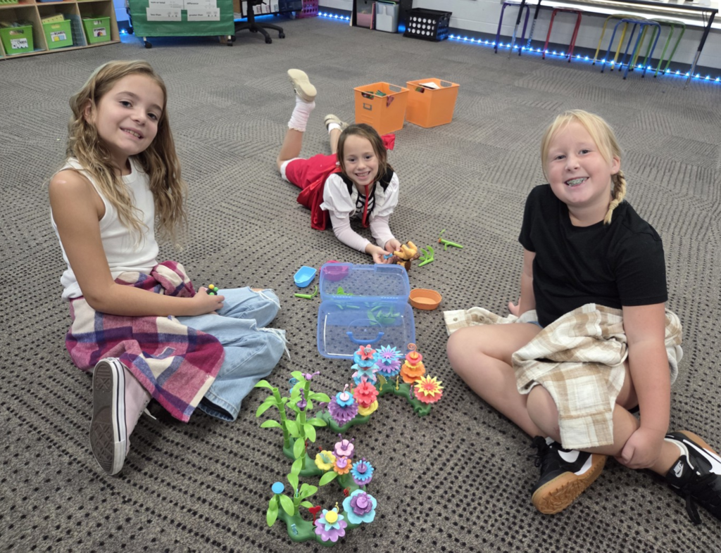 Three smiling second graders sitting on the floor working on activities during their celebration of the fairy tales and tall tales unit.