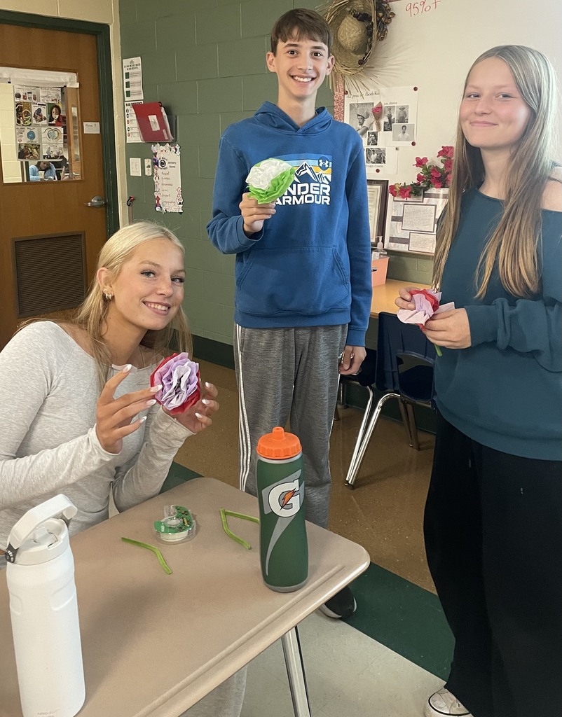 Three students smile and show off the paper flowers they created.