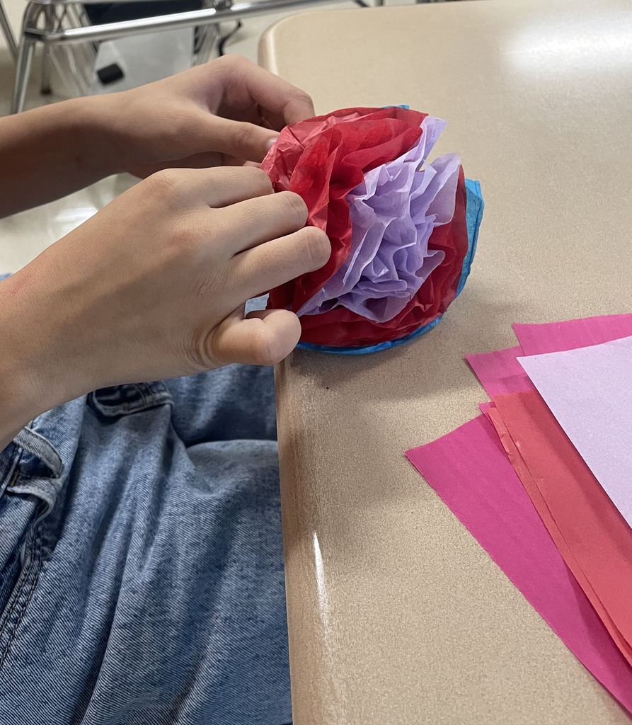 A close up photo of two hands making a paper flower out of tissue paper.