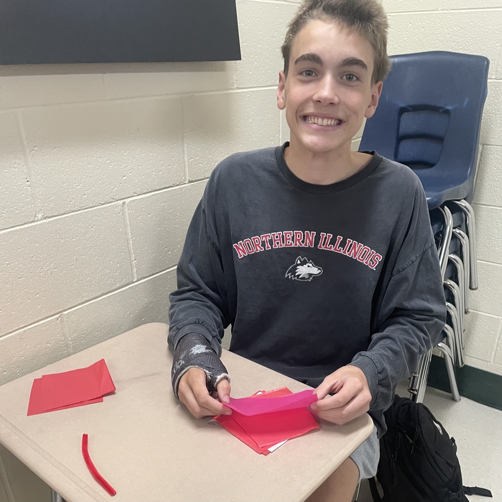 A smiling student sitting at a desk with tissue paper to make a paper flower.