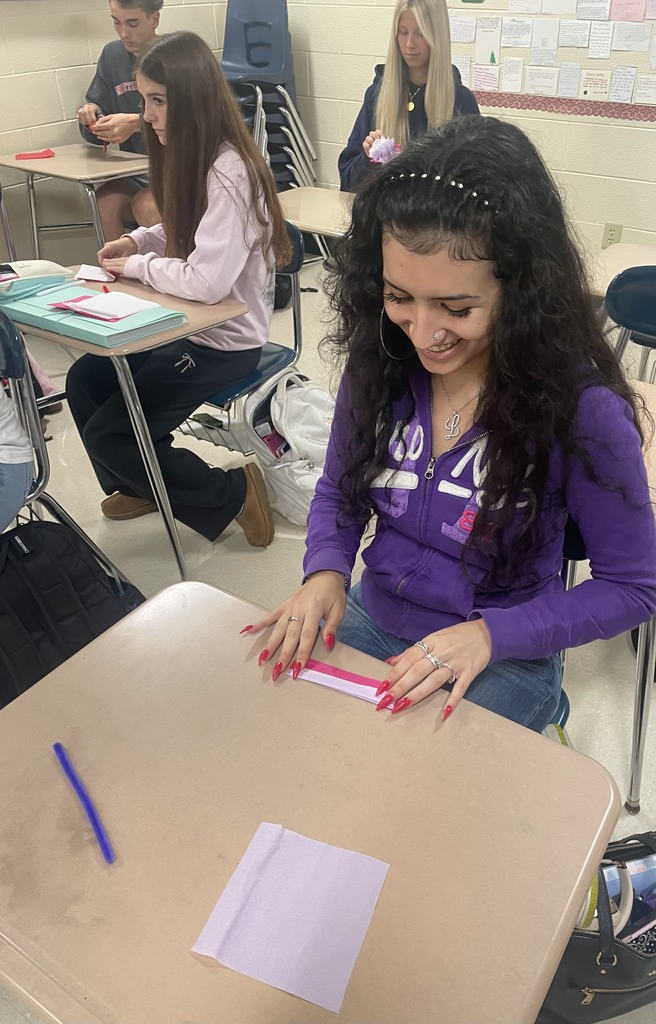 Student sitting at a desk working with tissue paper to make a paper flower.