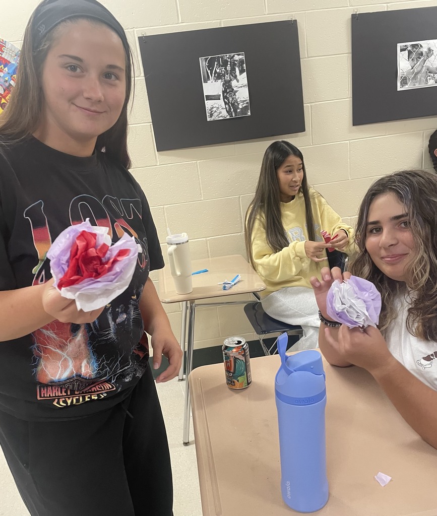 Two smiling students holding the paper flowers they created.
