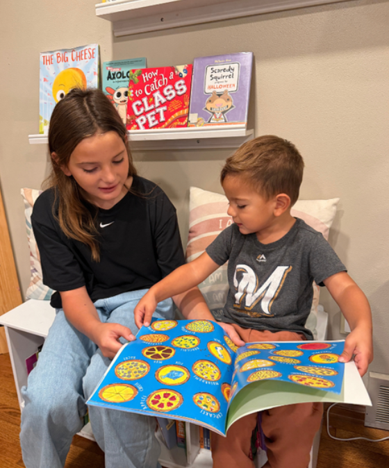 An older child and a younger child  looking at a book together.