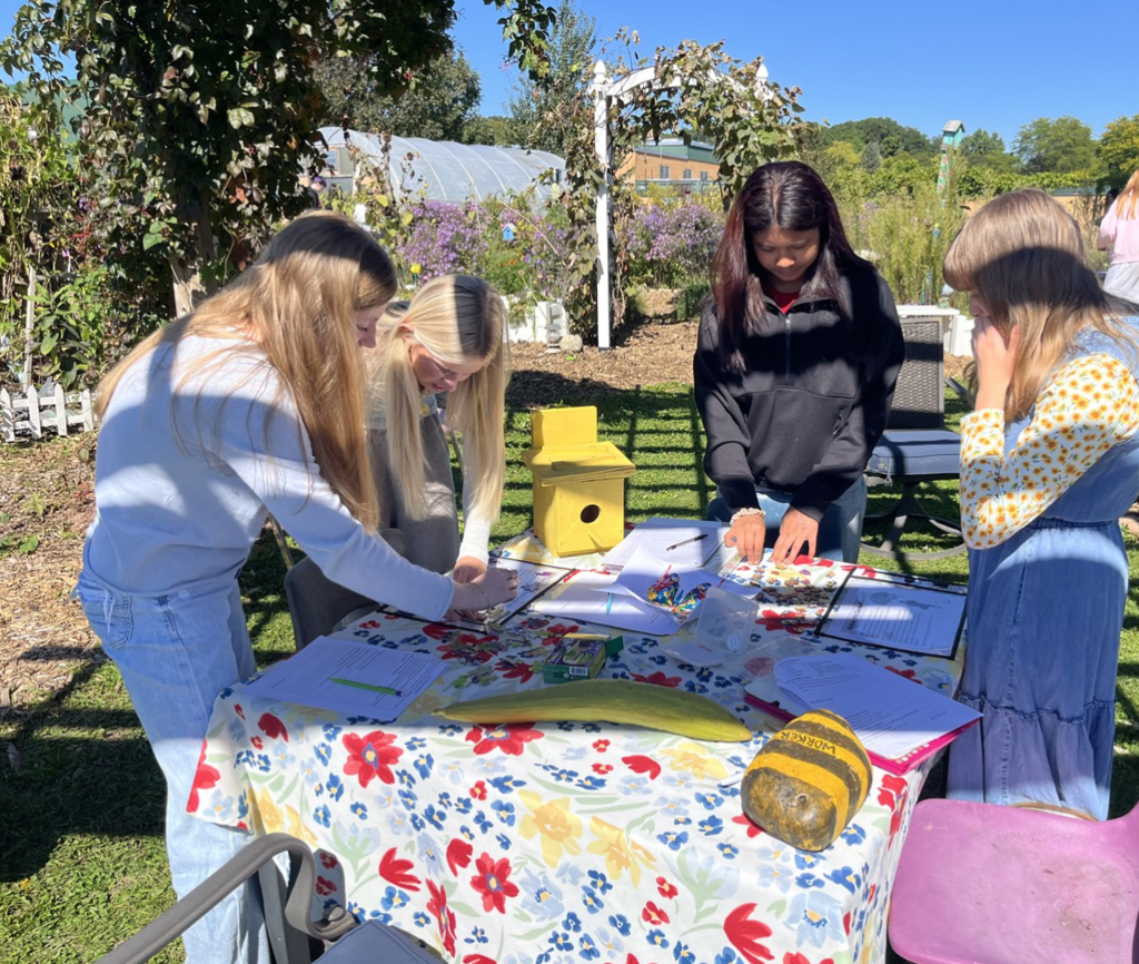 Three students are working at a table outside in the school garden on a sunny day.
