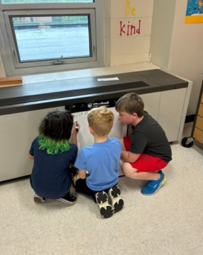 Three students from the back crouching in front of a small whiteboard conferring on a math equation..