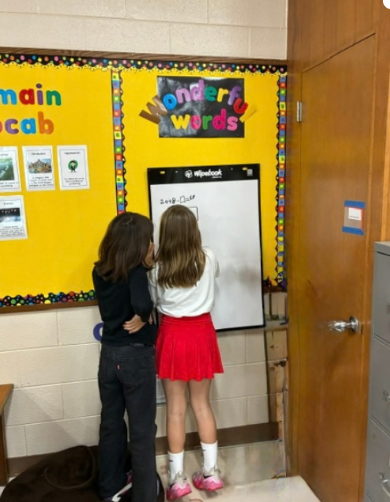 Two students from the back working on a white board on a wall.