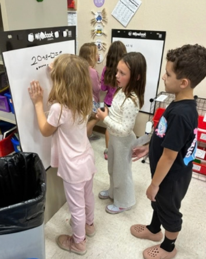 Three students collaborating on a math problem on a white board.