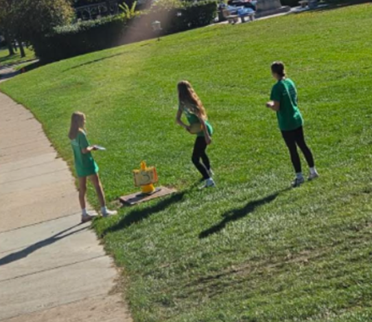 Three students stand in a grassy field preparing to throw their disks in a round of disk golf in PE.